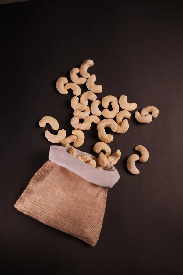 Whole cashews spilling out of a jute pouch onto dark stone